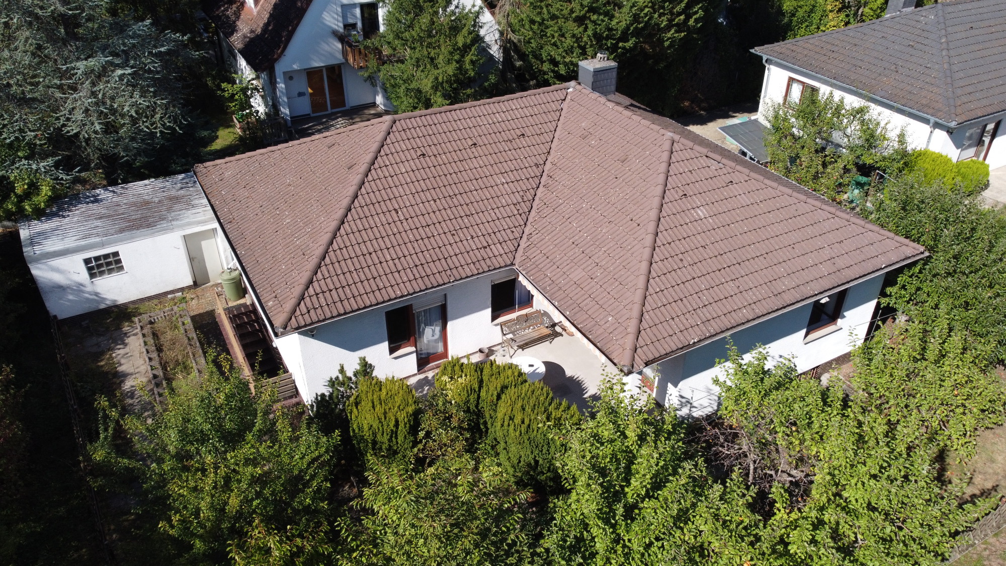 Einfamilienhaus mit braunem Walmdach, Terrasse und umliegendem Garten, aus der Vogelperspektive.