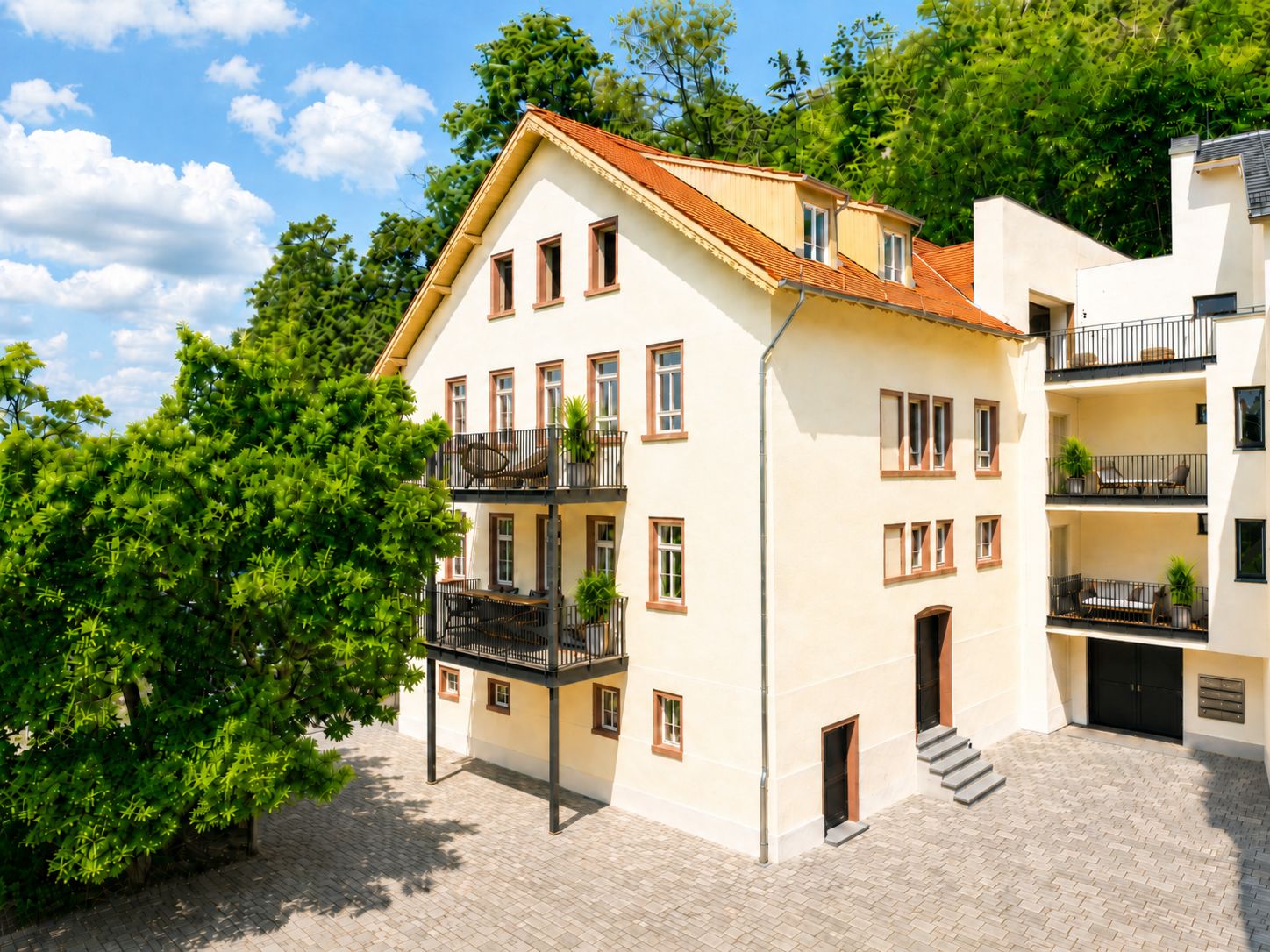 Helles Wohnhaus mit Balkonen, großem Fenster und Innenhof, umgeben von Bäumen.