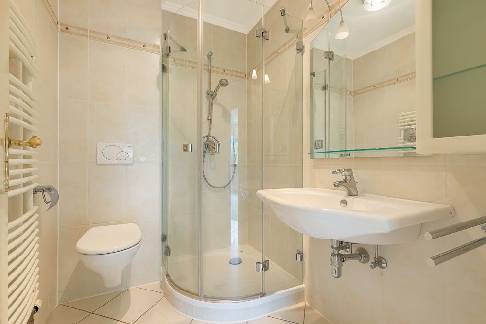 Helles Badezimmer mit Dusche, Wand-WC, Waschbecken und Handtuchheizung.