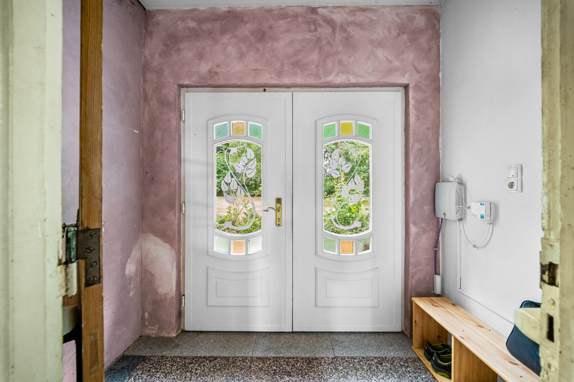 Eingangsbereich mit doppelflügeliger weißer Tür und Holzbank an der rechten Wand.
