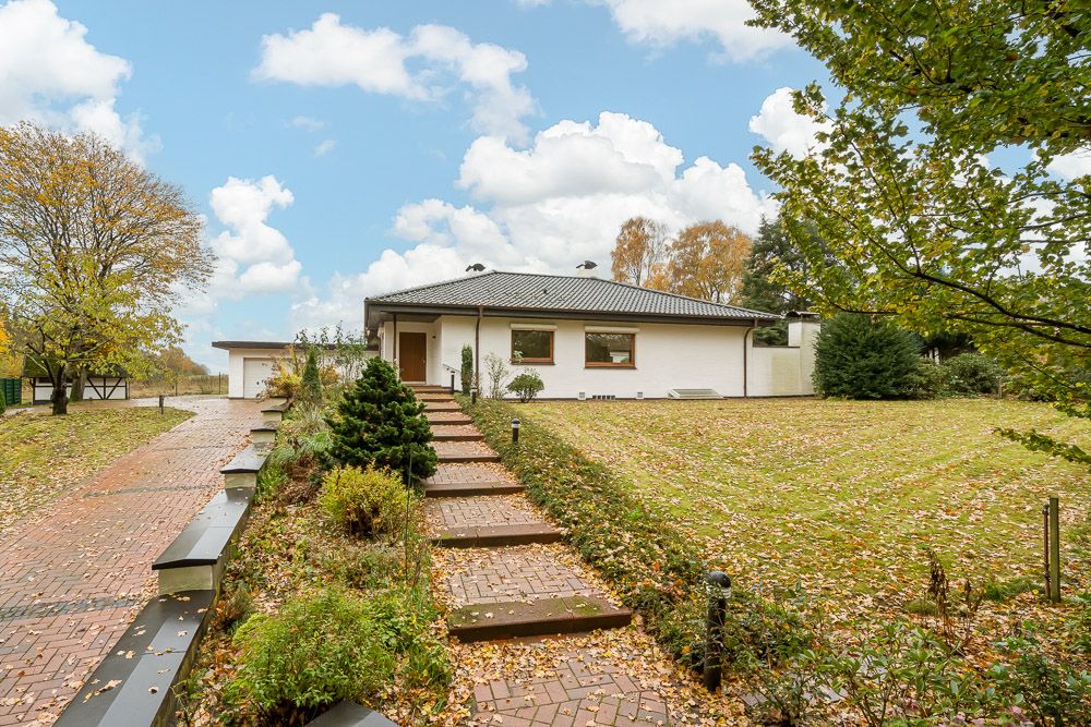 Einfamilienhaus mit grauem Dach und großem Garten, Weg und Stufen führen zum Eingang.