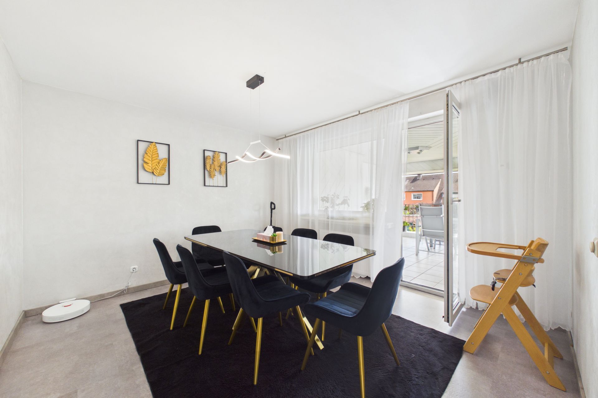 Esszimmer mit schwarzem Tisch, sechs Stühlen, Kinderhochstuhl und Zugang zum Balkon.