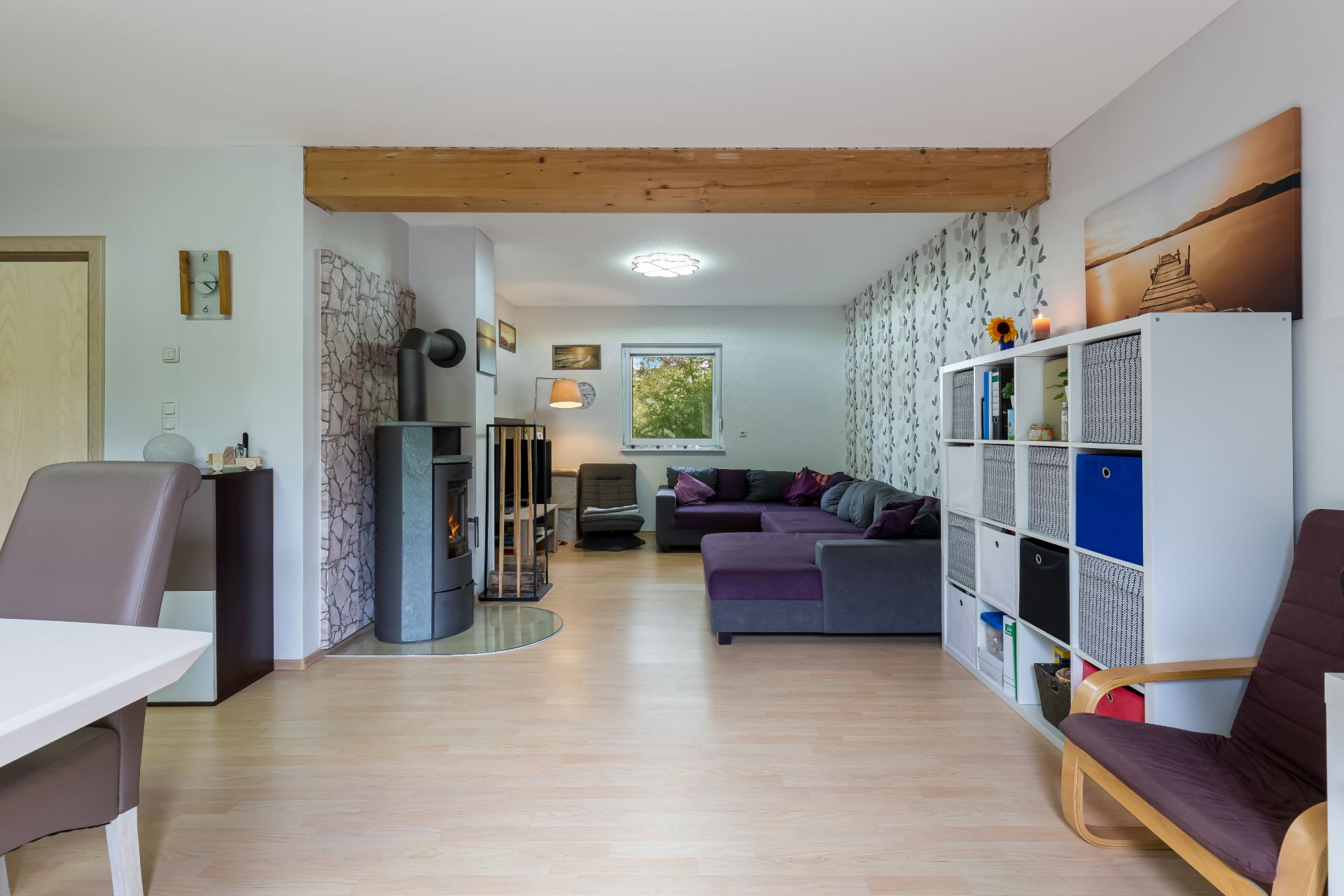 Modernes Wohnzimmer mit Ecksofa, Holzofen, Regal und großem Fenster.