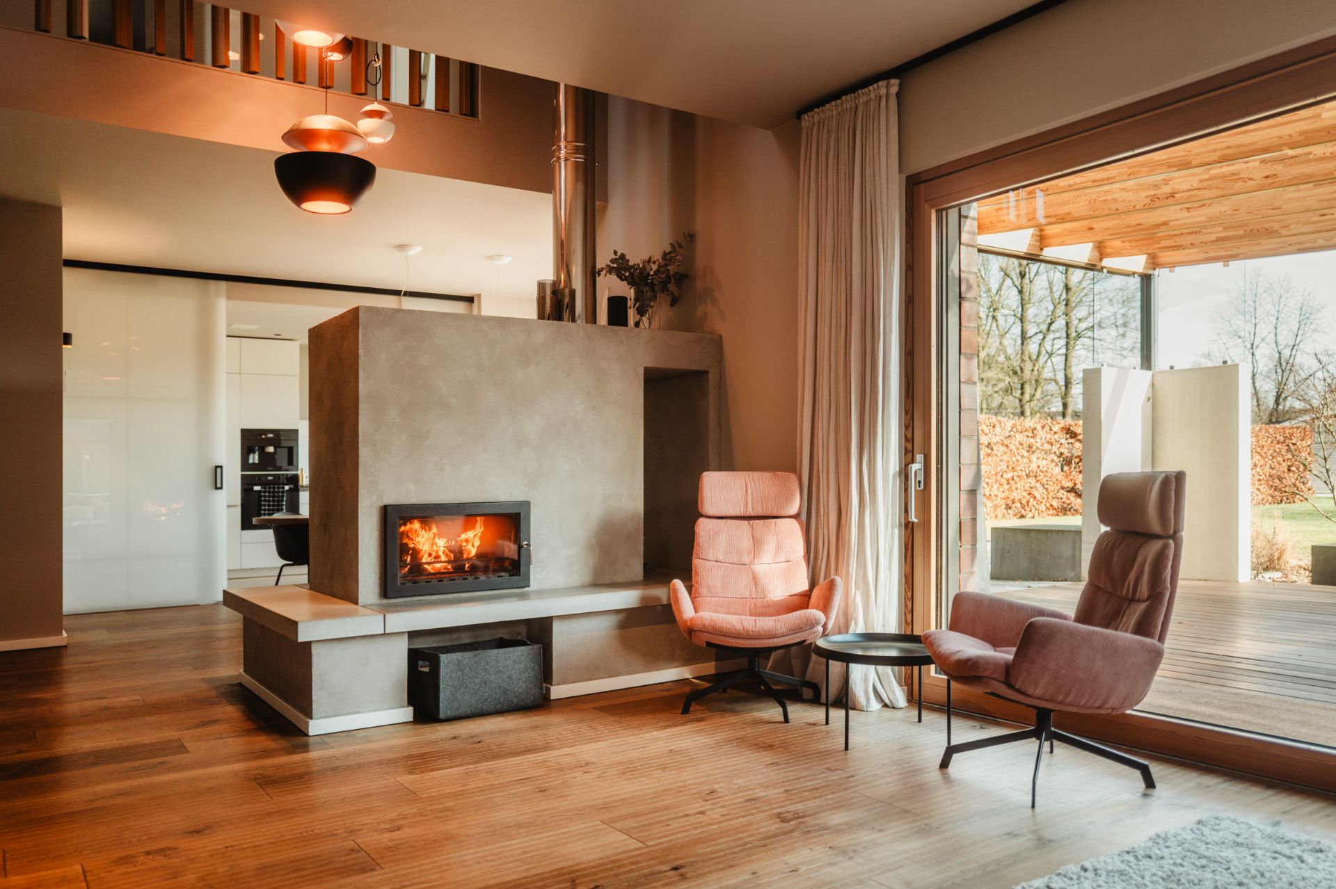 Wohnzimmer mit Kamin, zwei rosafarbenen Sesseln und großem Fenster zur Terrasse.