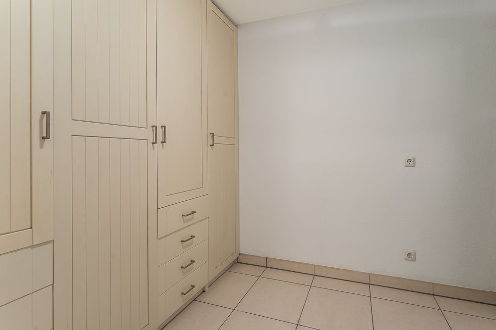 Raum mit Einbauschränken aus Holz und gefliesten Boden, helle Wände.