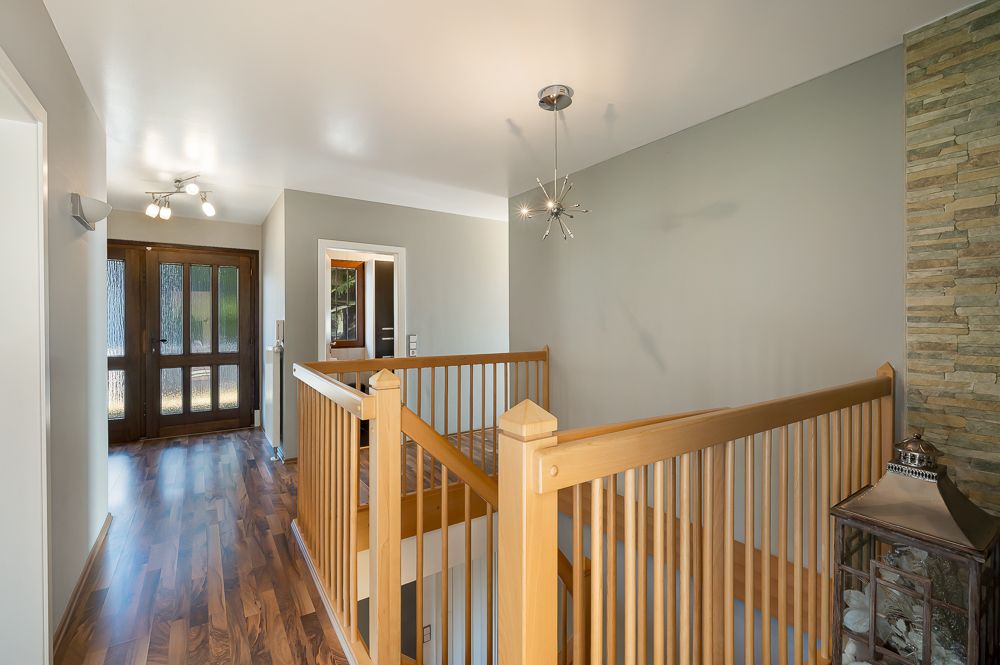 Flur mit Holzboden, Holzgeländer und moderner Deckenleuchte, Steindekor an der Wand.