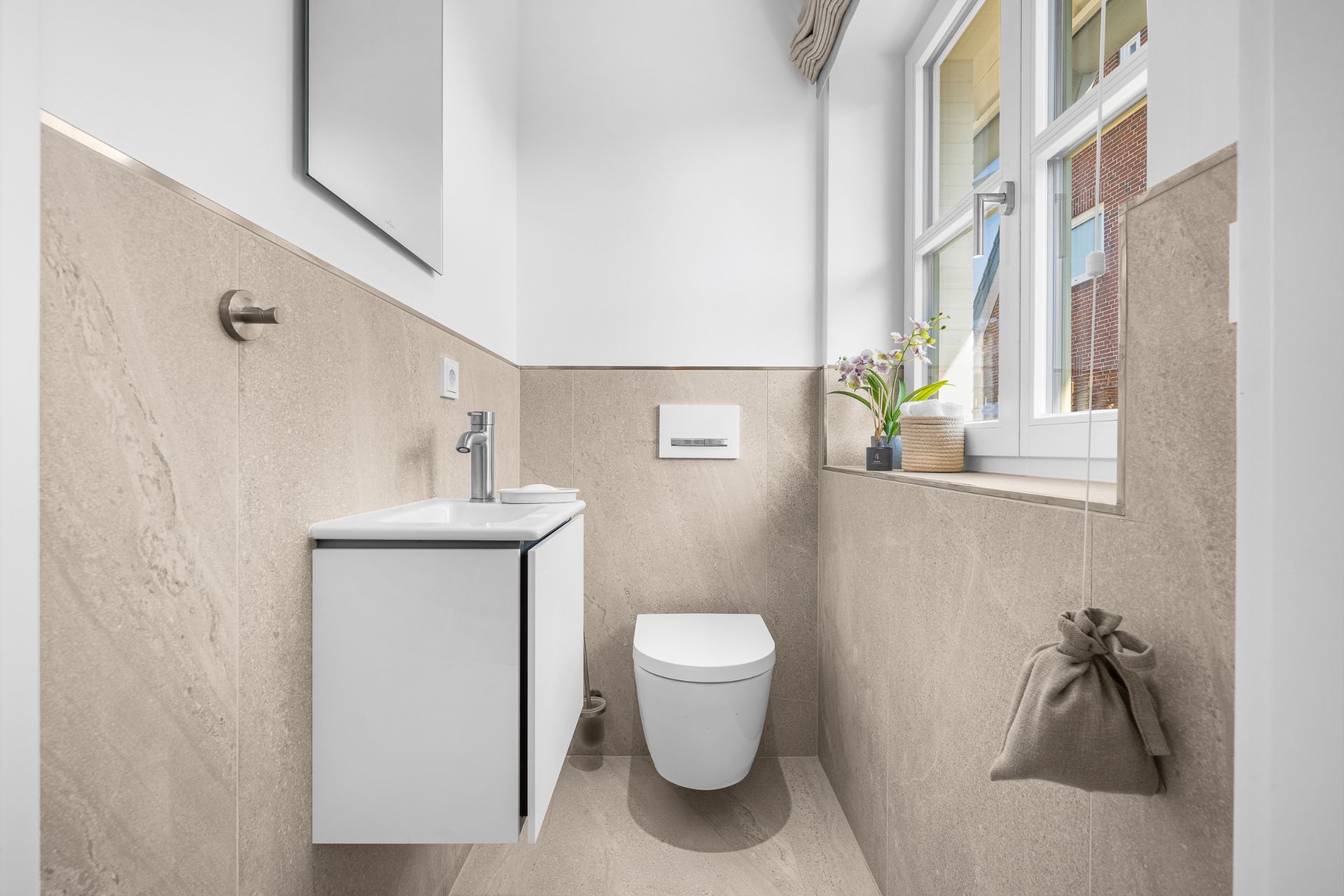 Modernes kleines Bad mit WC, Waschbecken, Spiegel und Fenster, beige gefliest.