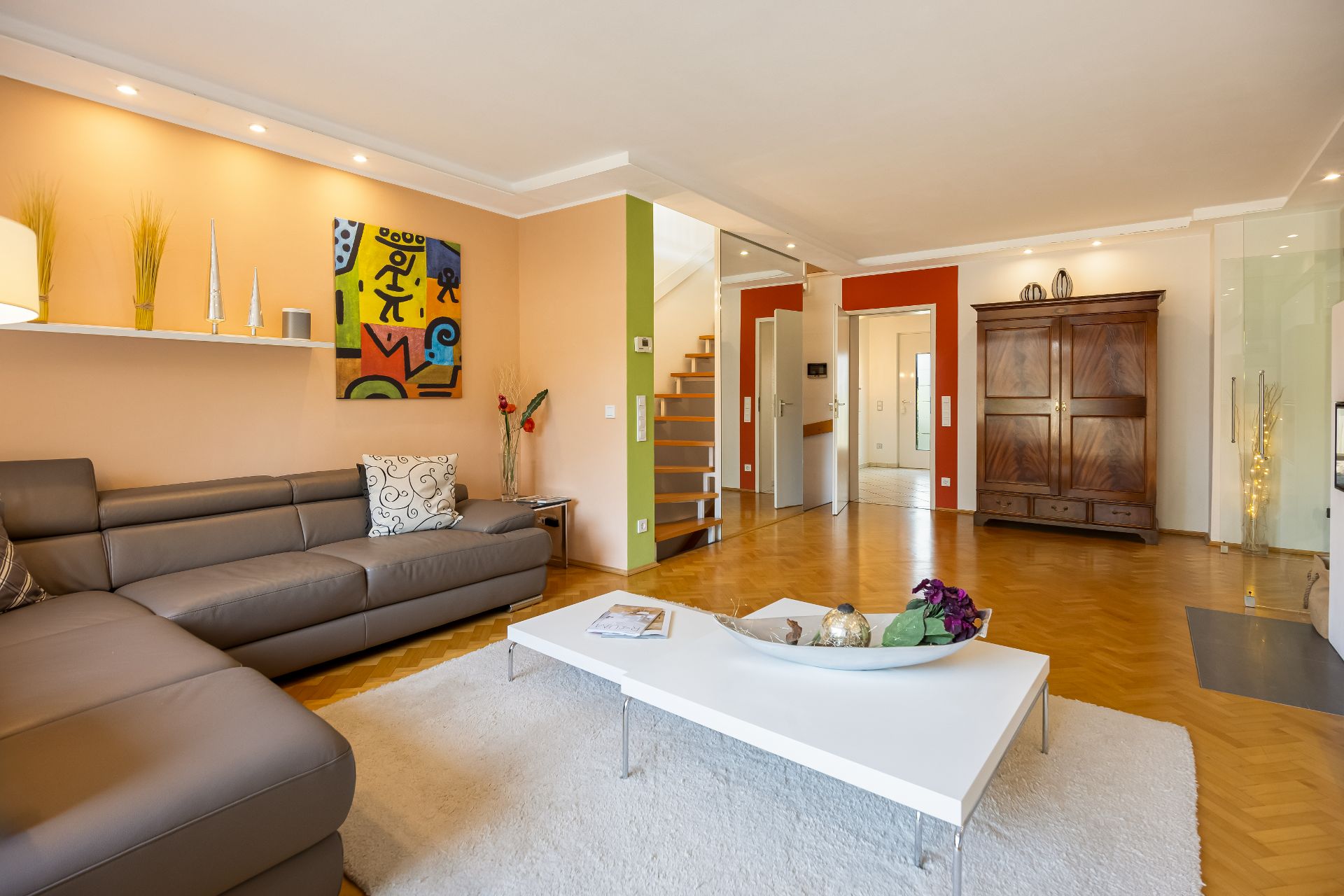 Modernes Wohnzimmer mit grauem Sofa, weißem Couchtisch und bunter Wandkunst.