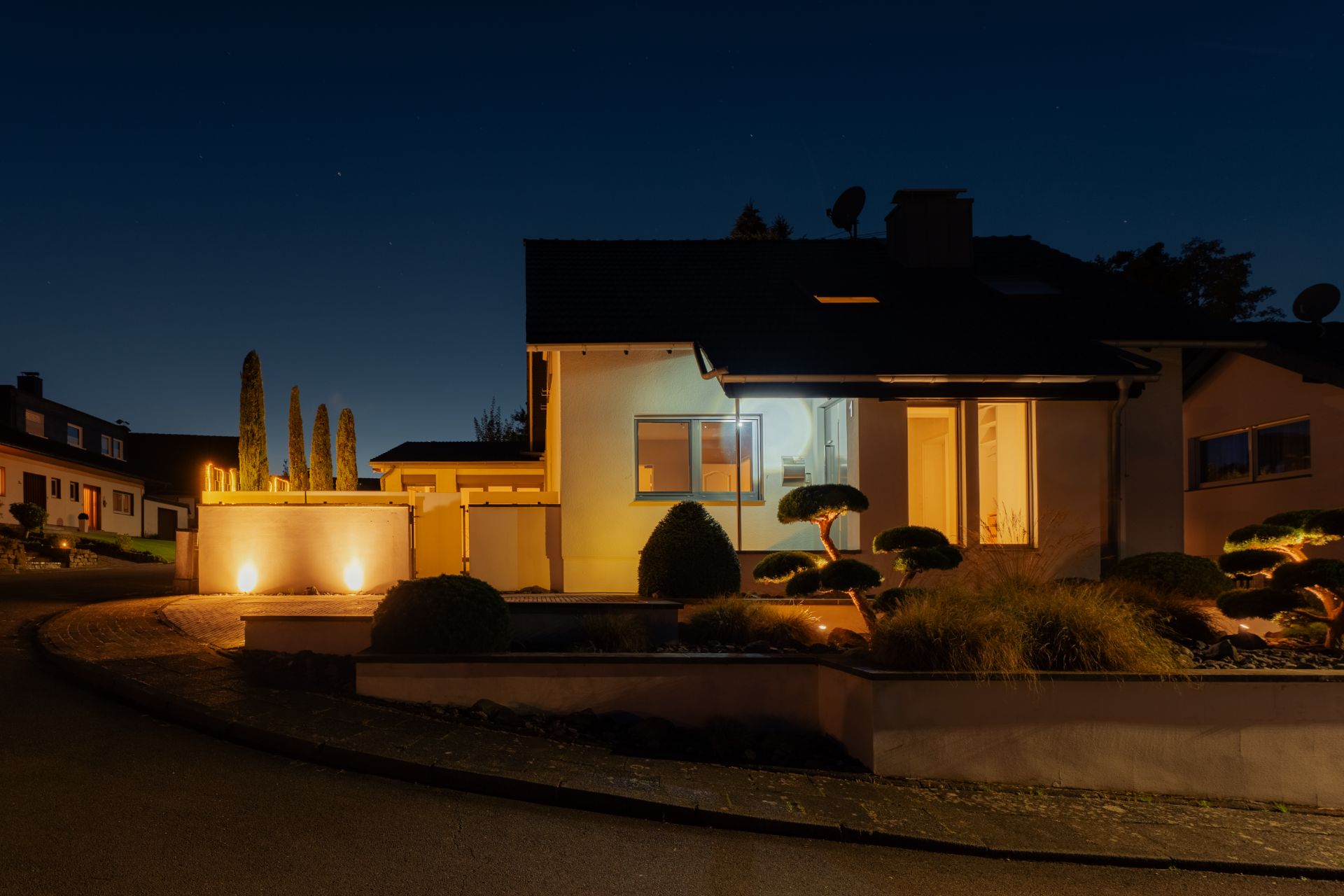 Modernes Wohnhaus bei Nacht mit beleuchtetem Garten und gepflegtem Vorgarten.
