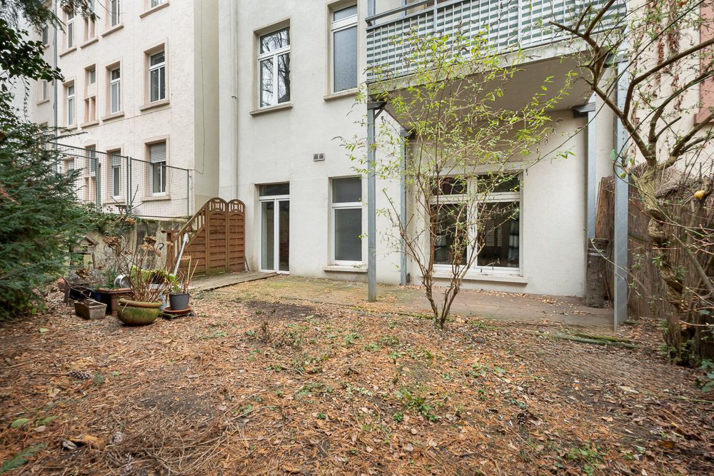 Blick auf einen kleinen, teils bepflanzten Hinterhof mit Terrasse und Zugang zu einer Wohnung.