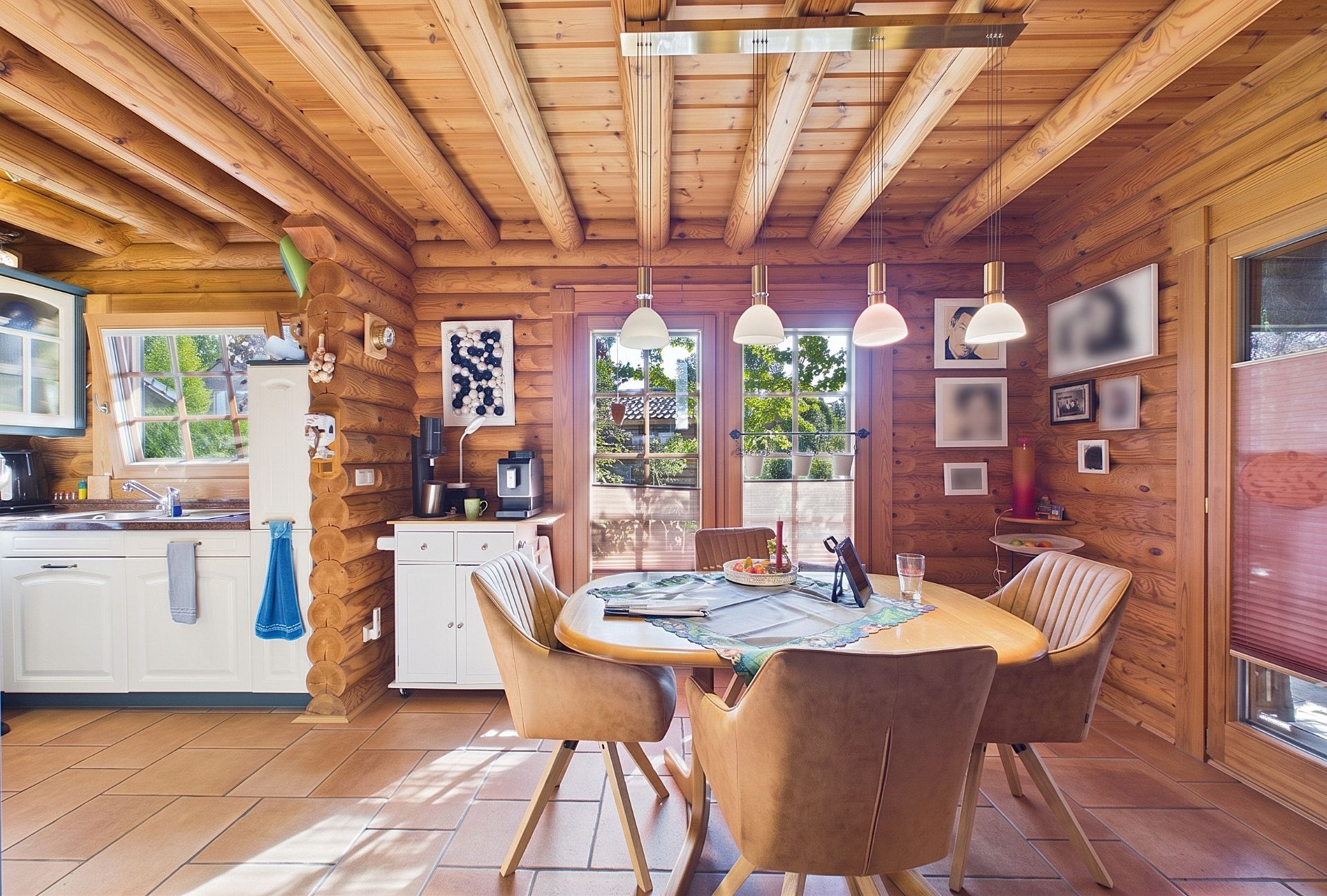 Helles Esszimmer mit Holzwänden, rundem Tisch, vier Stühlen und angrenzender Küchenzeile.