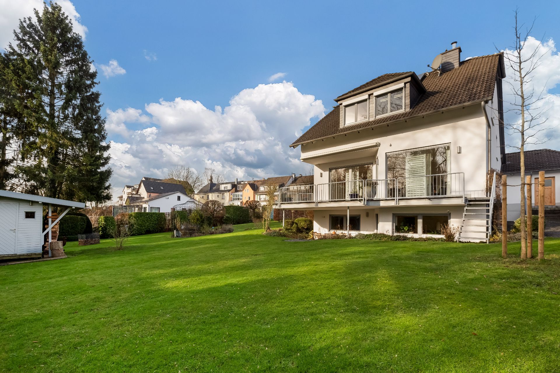 Modernes Einfamilienhaus mit großem, gepflegtem Garten und Gartenhaus bei Sonnenschein.