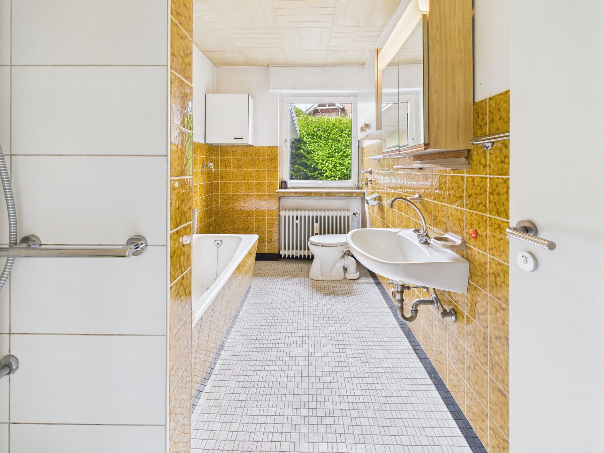 Helles Badezimmer mit gelben Fliesen, Badewanne, Waschbecken, Toilette und Fenster.