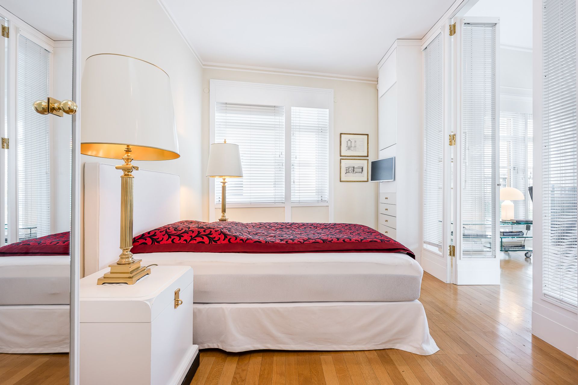 Helles Schlafzimmer mit Doppelbett, Nachttischlampe, Holzboden und großen Fenstern.