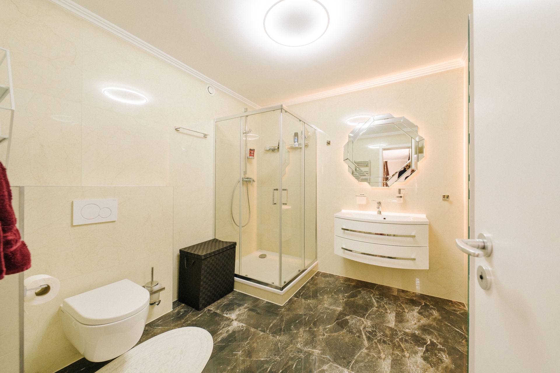 Modernes Badezimmer mit Dusche, WC, Waschtisch mit Spiegel und gemustertem Boden.