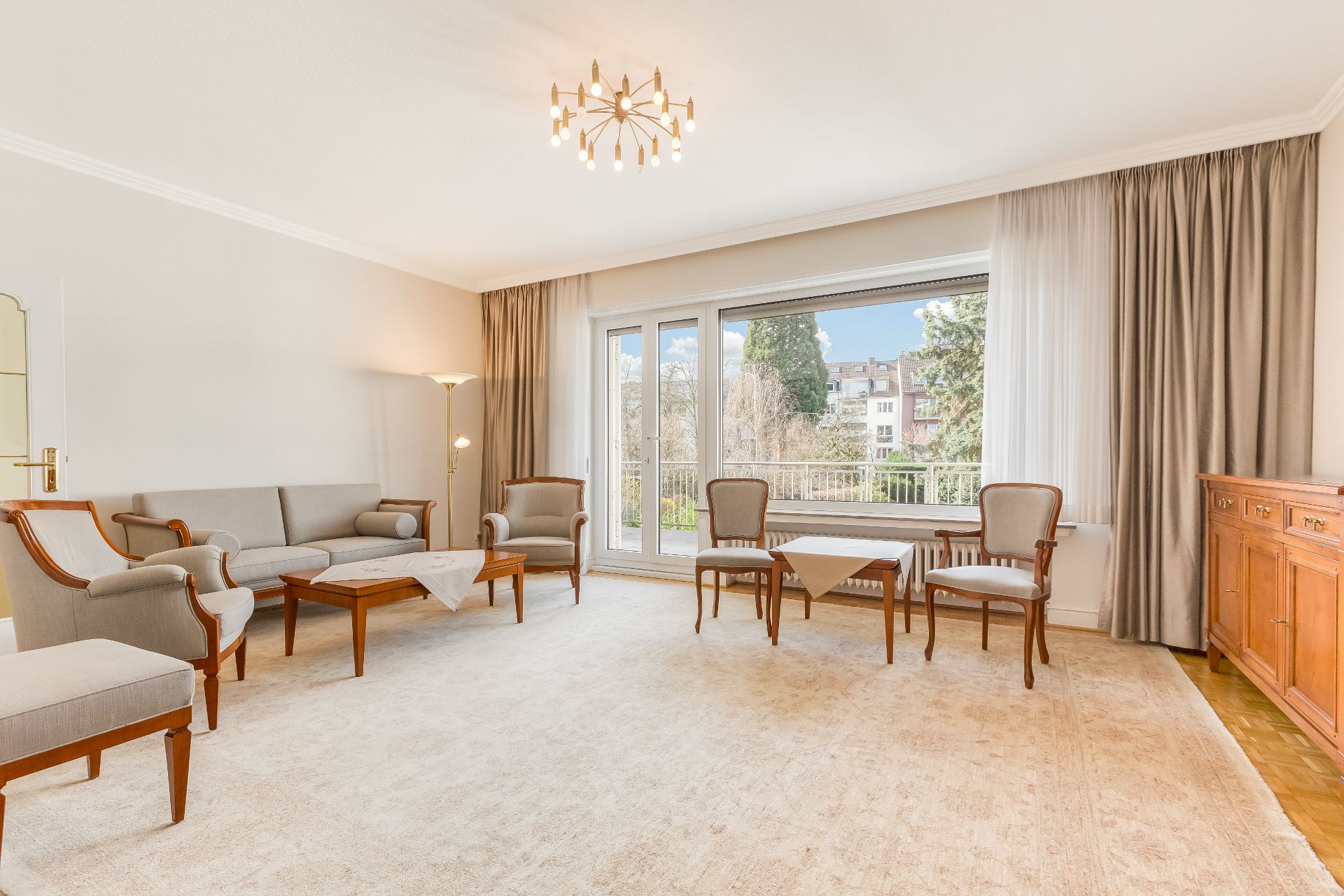 Helles Wohnzimmer mit Holzmöbeln, Teppich, großem Fenster und Blick auf Bäume.