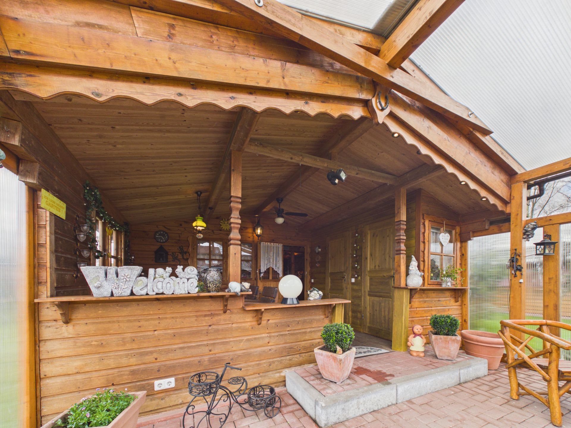 Überdachte Holzveranda mit Dekorationen und Pflanzen in Töpfen.