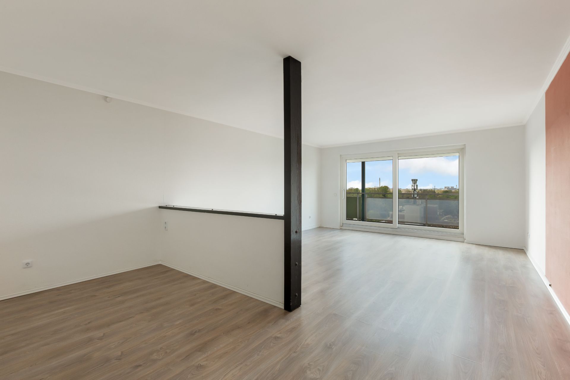 Helles Wohnzimmer mit Holzfußboden, großem Fenster und schwarzer Säule in der Mitte.