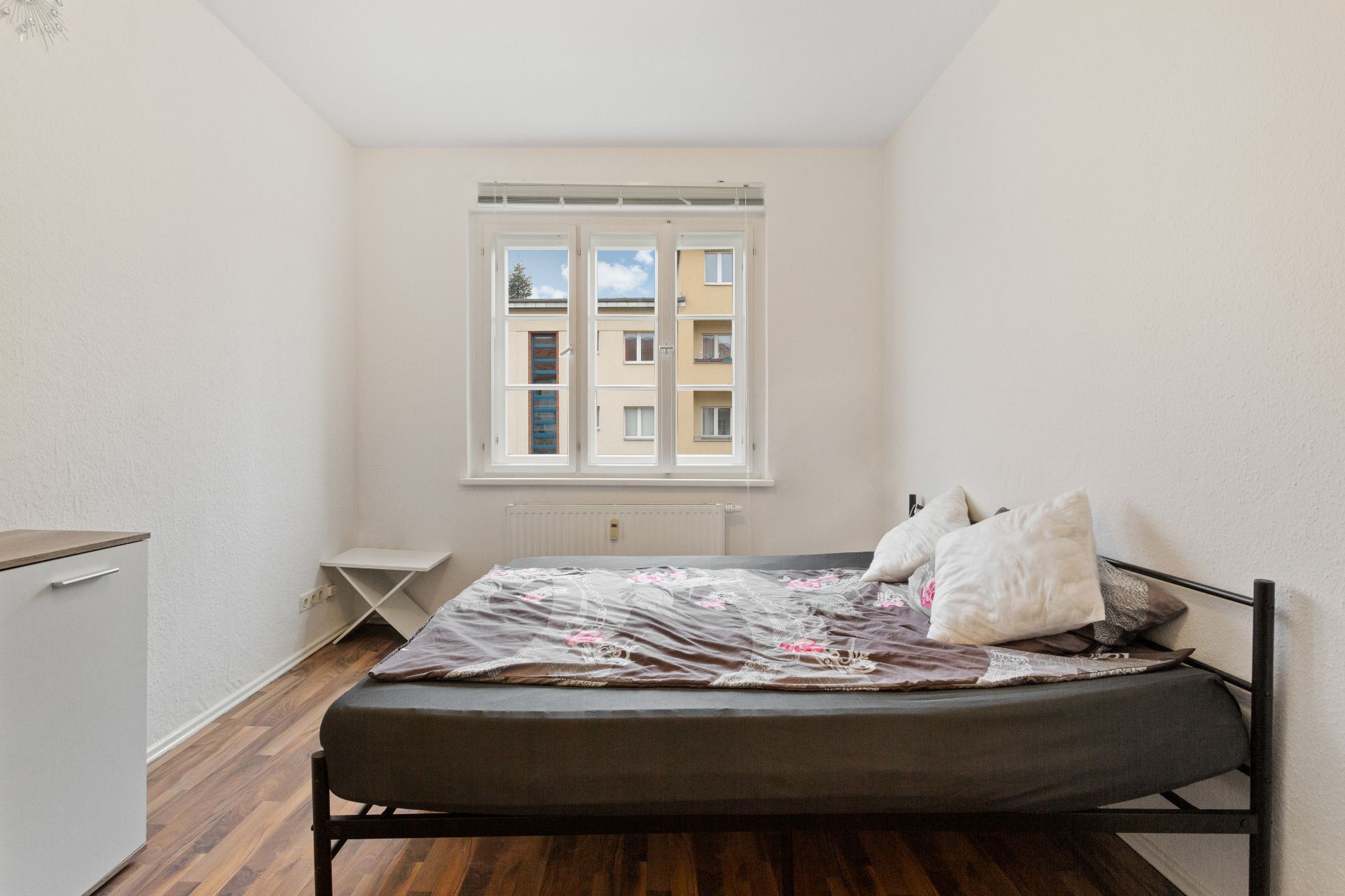 Helles Schlafzimmer mit Doppelbett, zwei Kissen, Fenster und Holzboden.