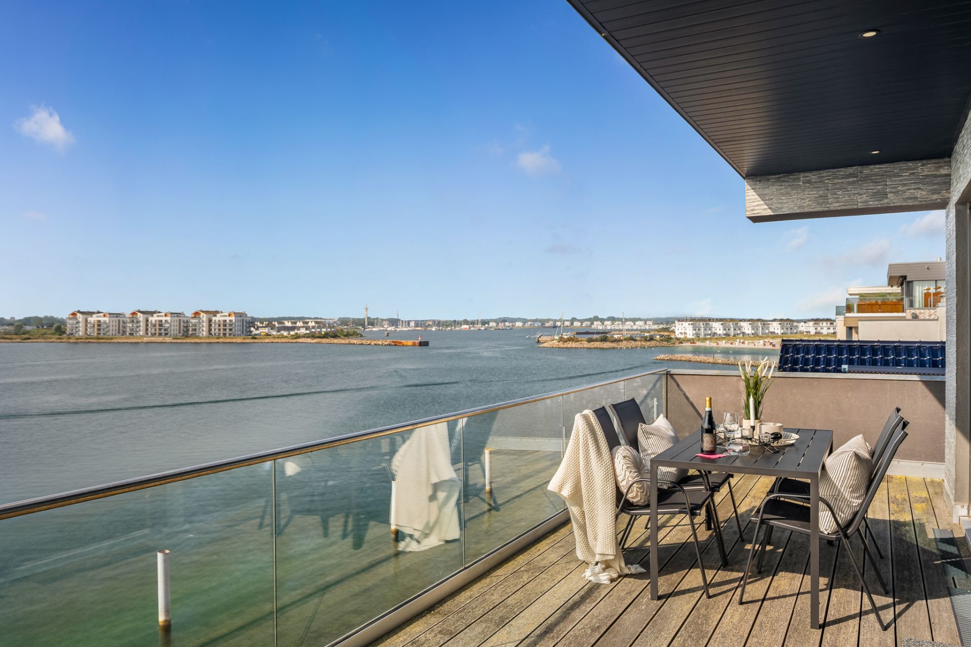 Balkon mit Glasgeländer, Esstisch und Blick auf Wasser und gegenüberliegende Gebäude.