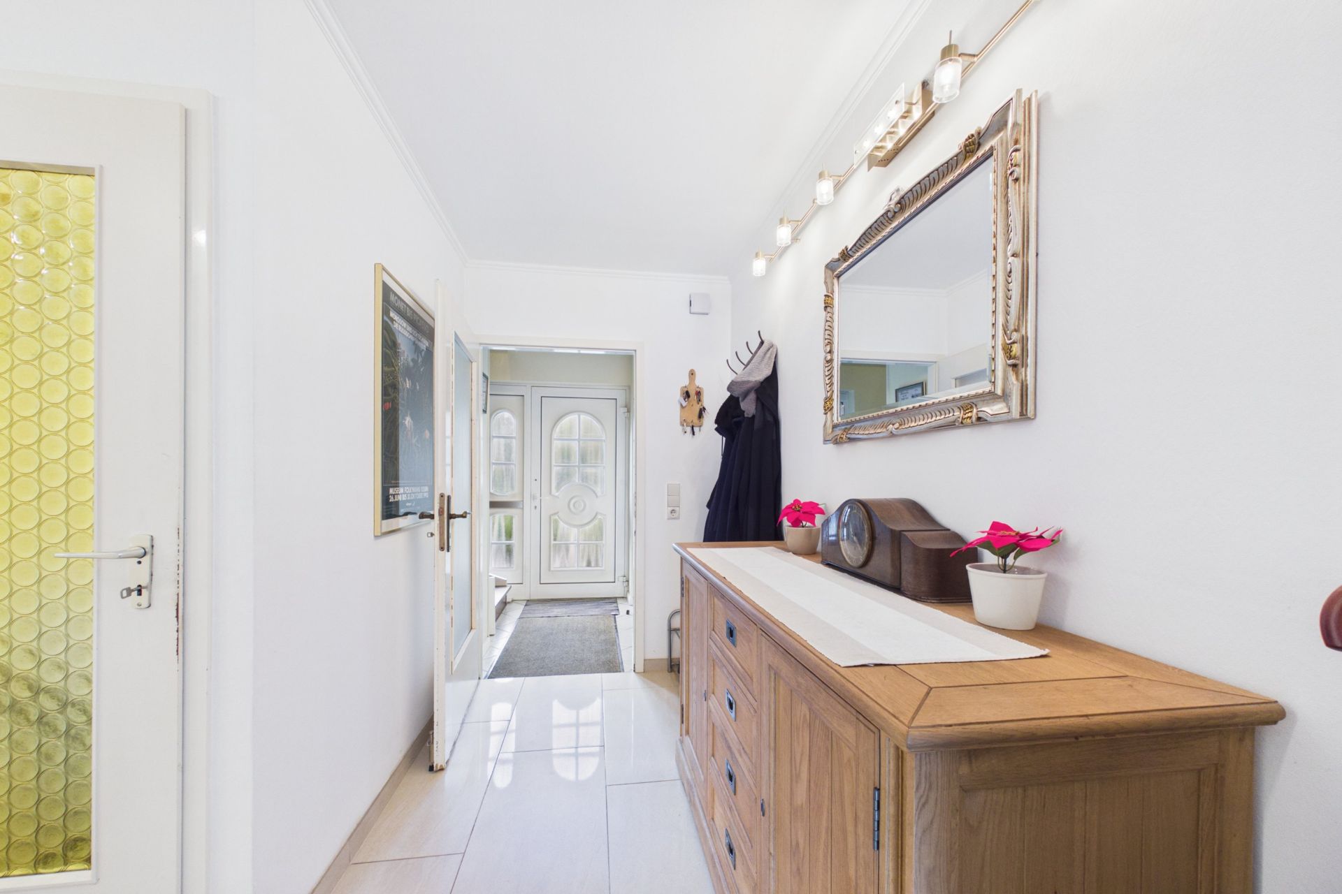 Heller Flur mit Holzkommode, Spiegel und Garderobe, Blick auf die Haustür.