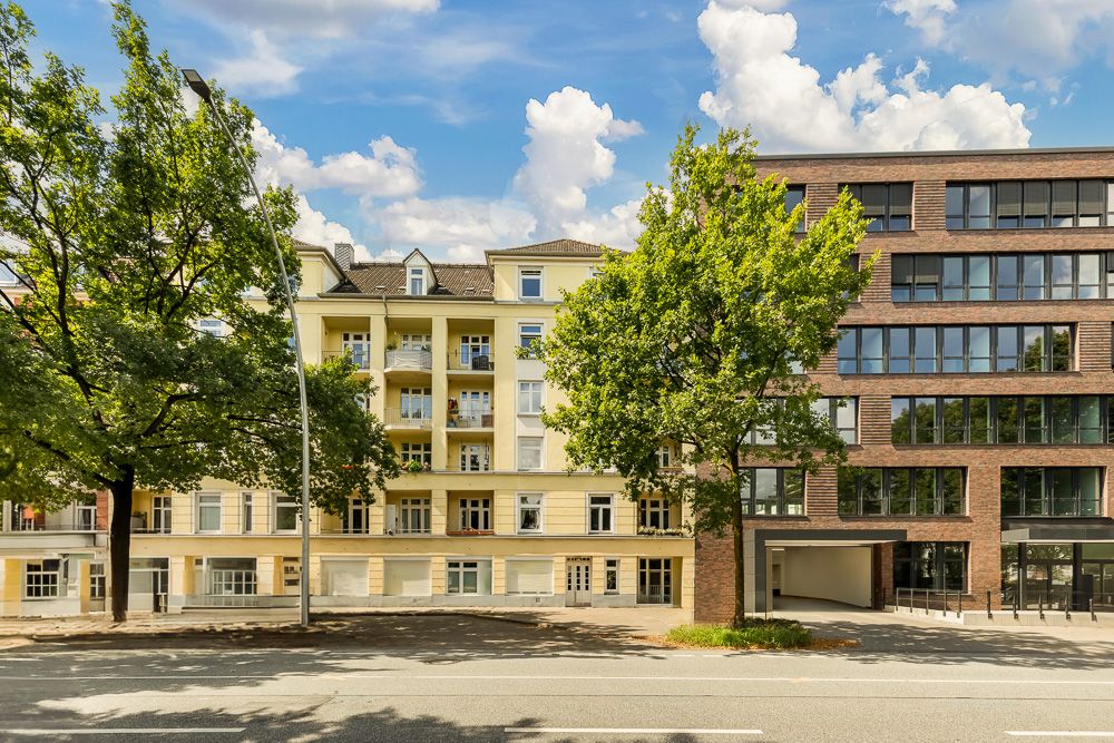 Mehrstöckiges Wohnhaus mit Balkonen und Bäumen an einer Straße.
