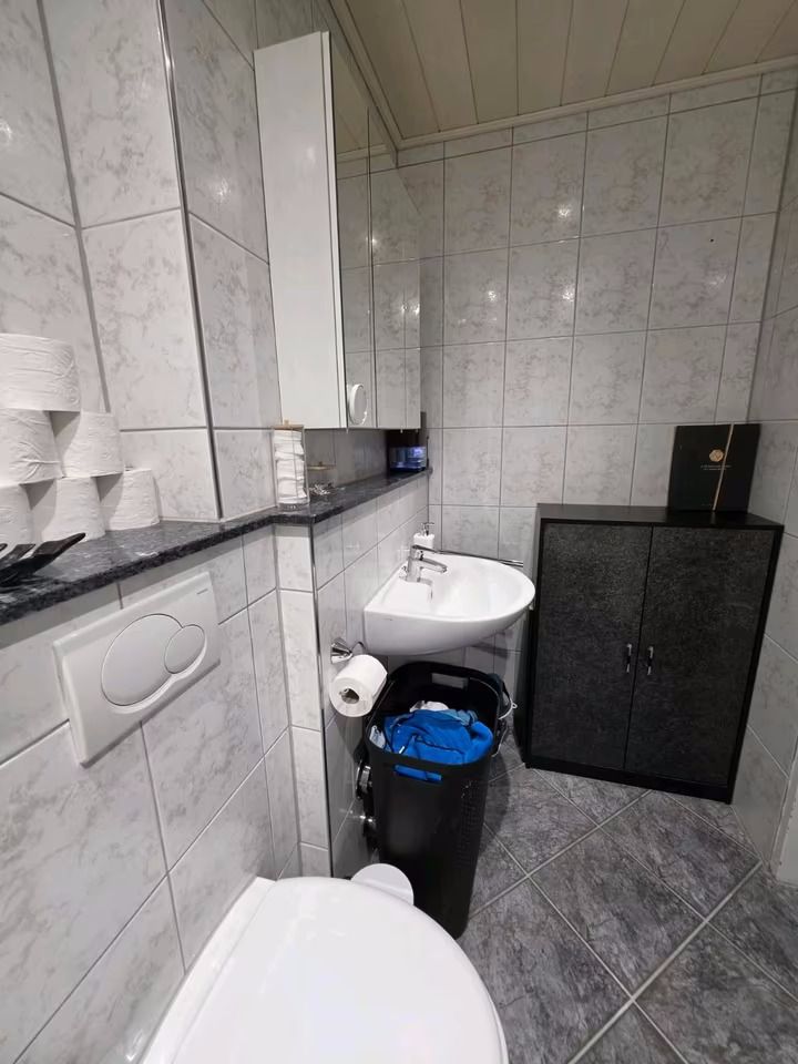 Kleines Badezimmer mit WC, Waschbecken, Spiegelschrank, Mülleimer und einem Schrank auf Fliesenboden.