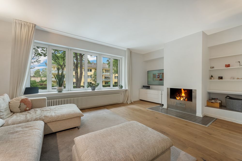 Helles Wohnzimmer mit großem Fenster, Kamin, Sofa und Holzfußboden.