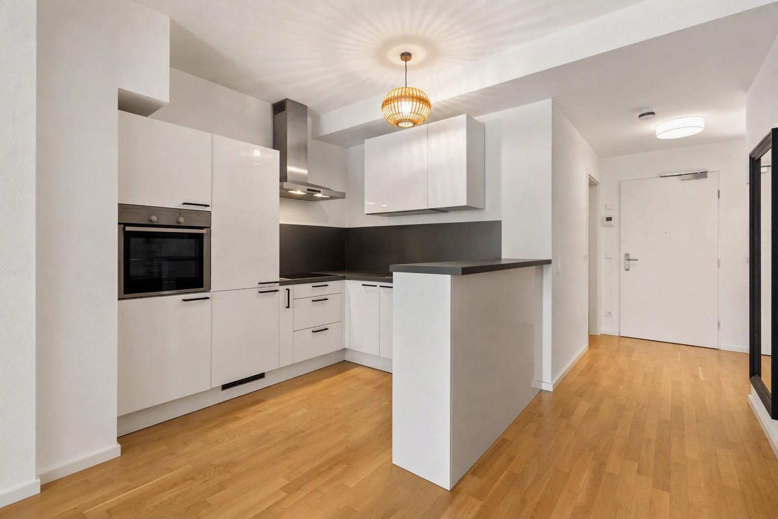 Helle moderne Einbauküche mit weißen Schränken und Holzfußboden in einer Wohnung.