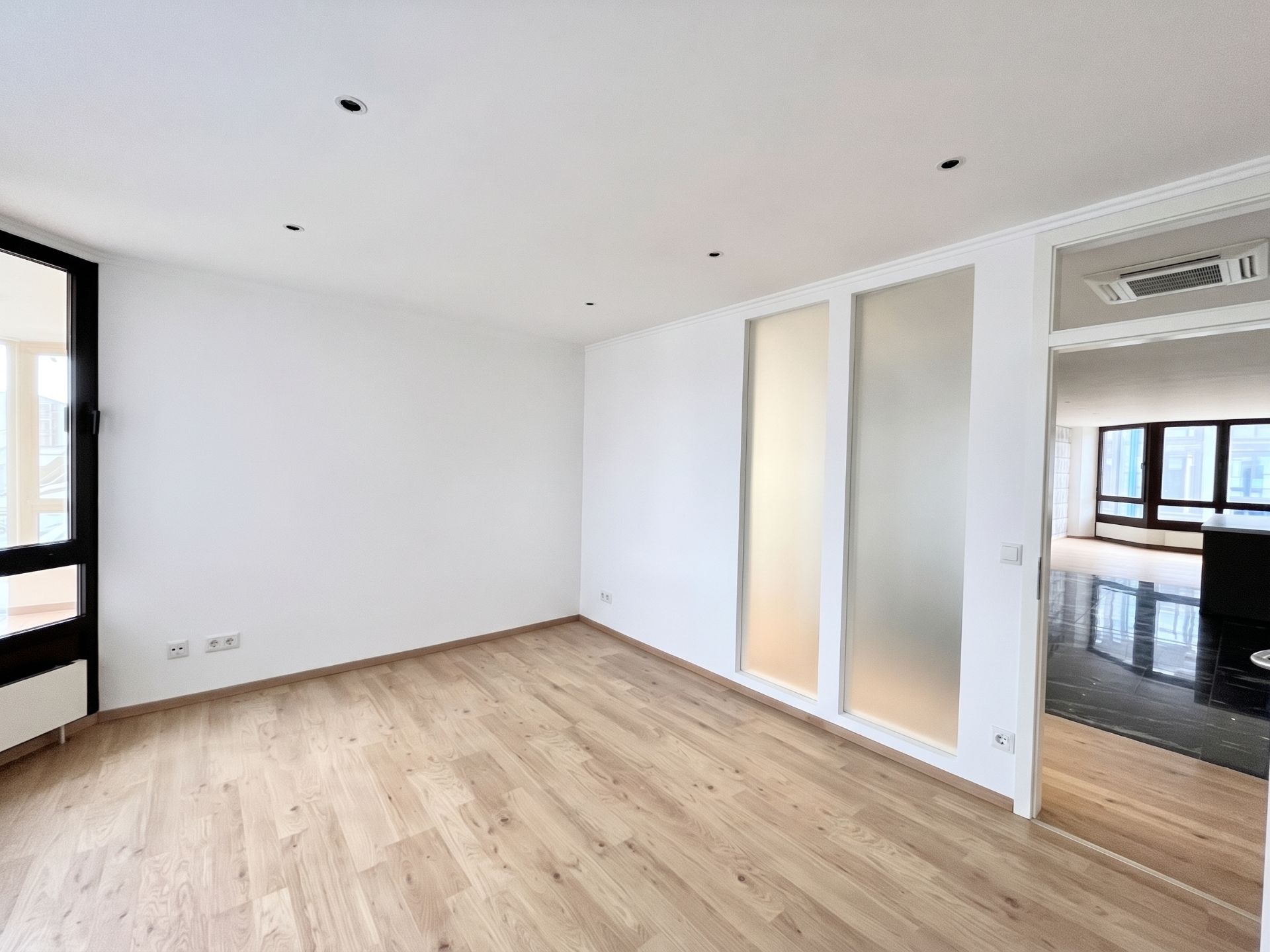 Heller Raum mit Holzfußboden, weißen Wänden und großen Fenstern.