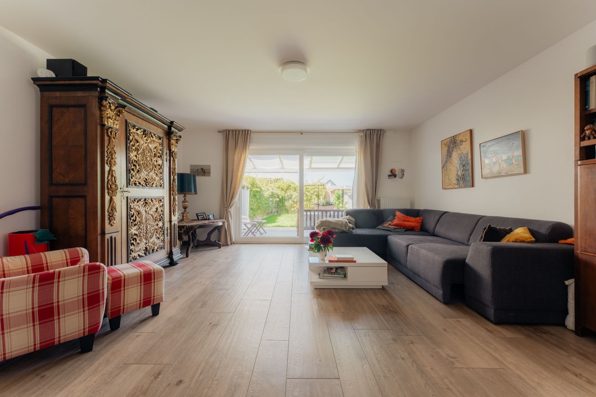 Helles Wohnzimmer mit grauem Sofa, gemustertem Sessel und großem Fenster zur Terrasse.