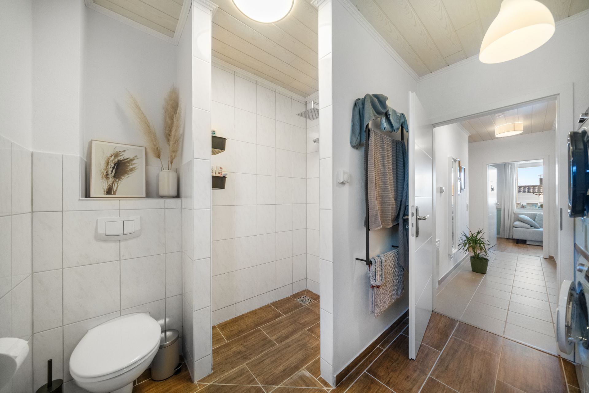Modernes Badezimmer mit offener Dusche, Toilette und Handtuchhaltern, Flur im Hintergrund.