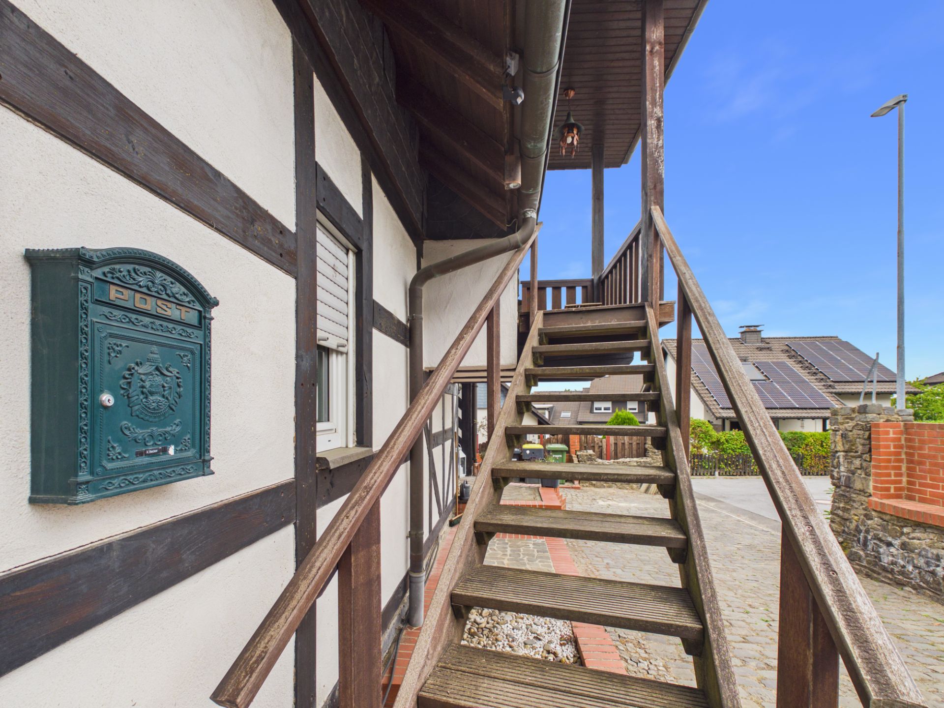 Holztreppe führt an Fachwerkhaus mit grünem Briefkasten im Außenbereich nach oben.