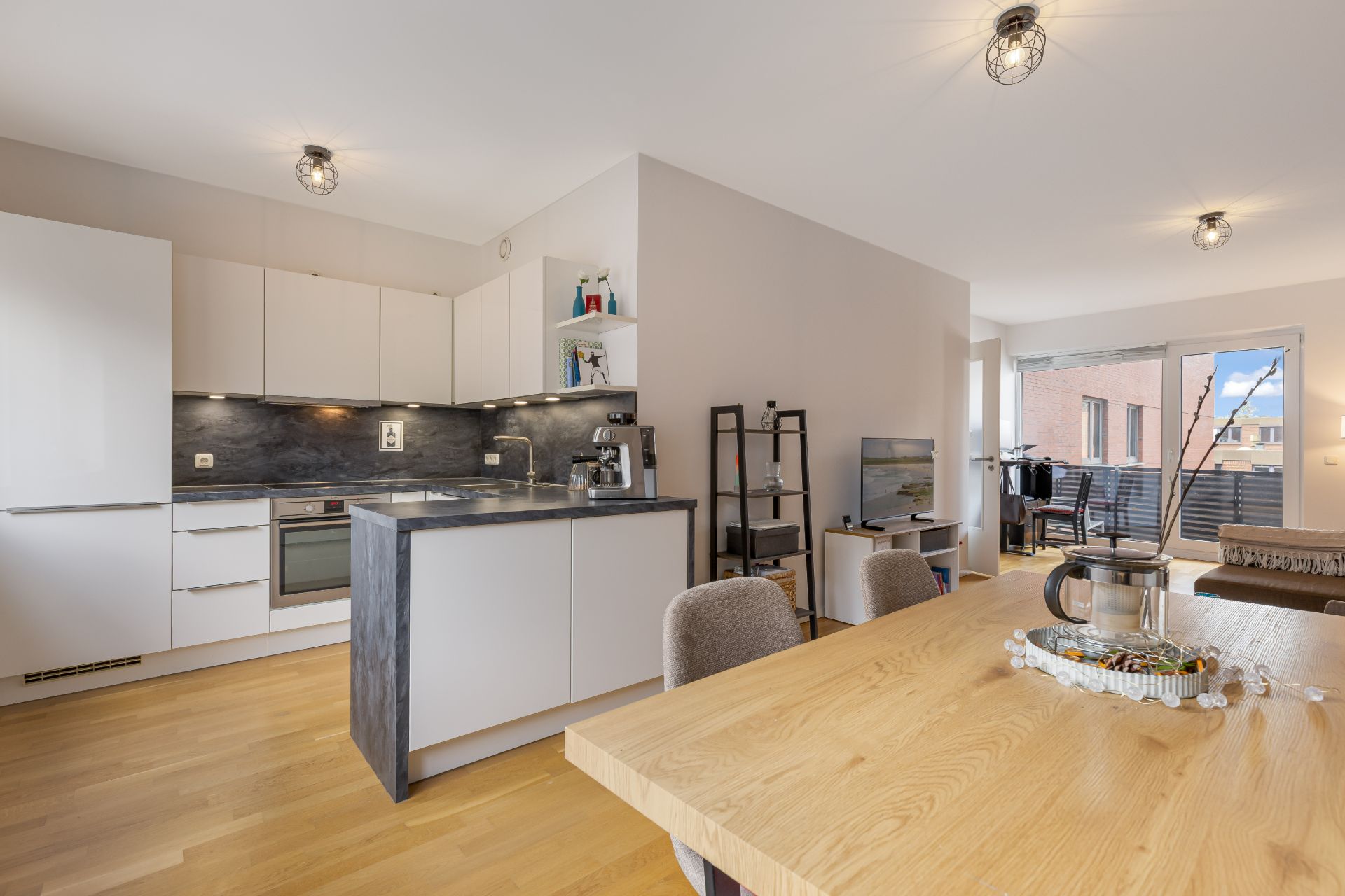 Moderne offene Küche mit Essbereich und Wohnzimmer, Holzboden und Zugang zu einem Balkon.