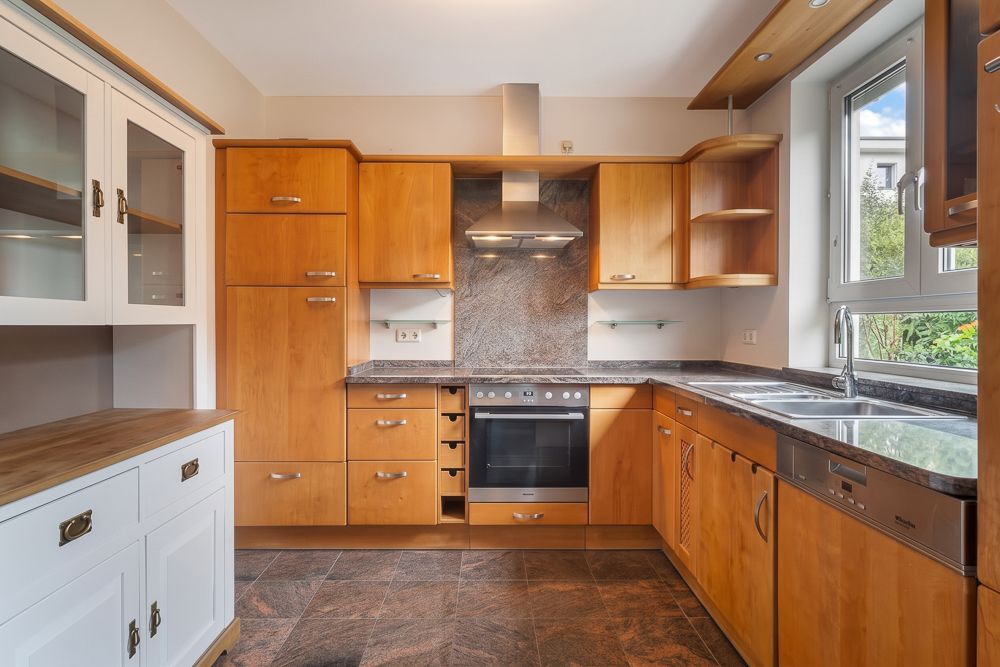 Helle Einbauküche mit Holzfronten, Elektroherd, Spüle und Fenster über der Arbeitsplatte.