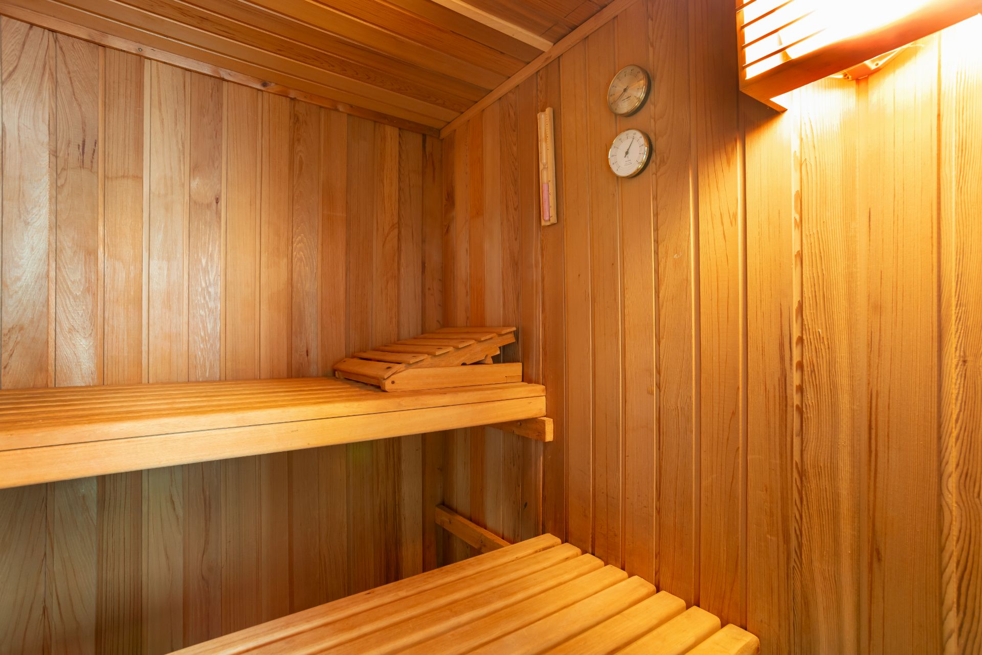 Innenansicht einer hölzernen Sauna mit zwei Bänken und Messinstrumenten an der Wand.