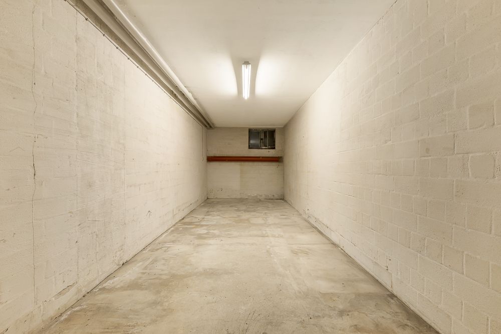 Leerer, schmaler Raum mit Betonboden, weißen Wänden und kleinem Fenster am Ende.