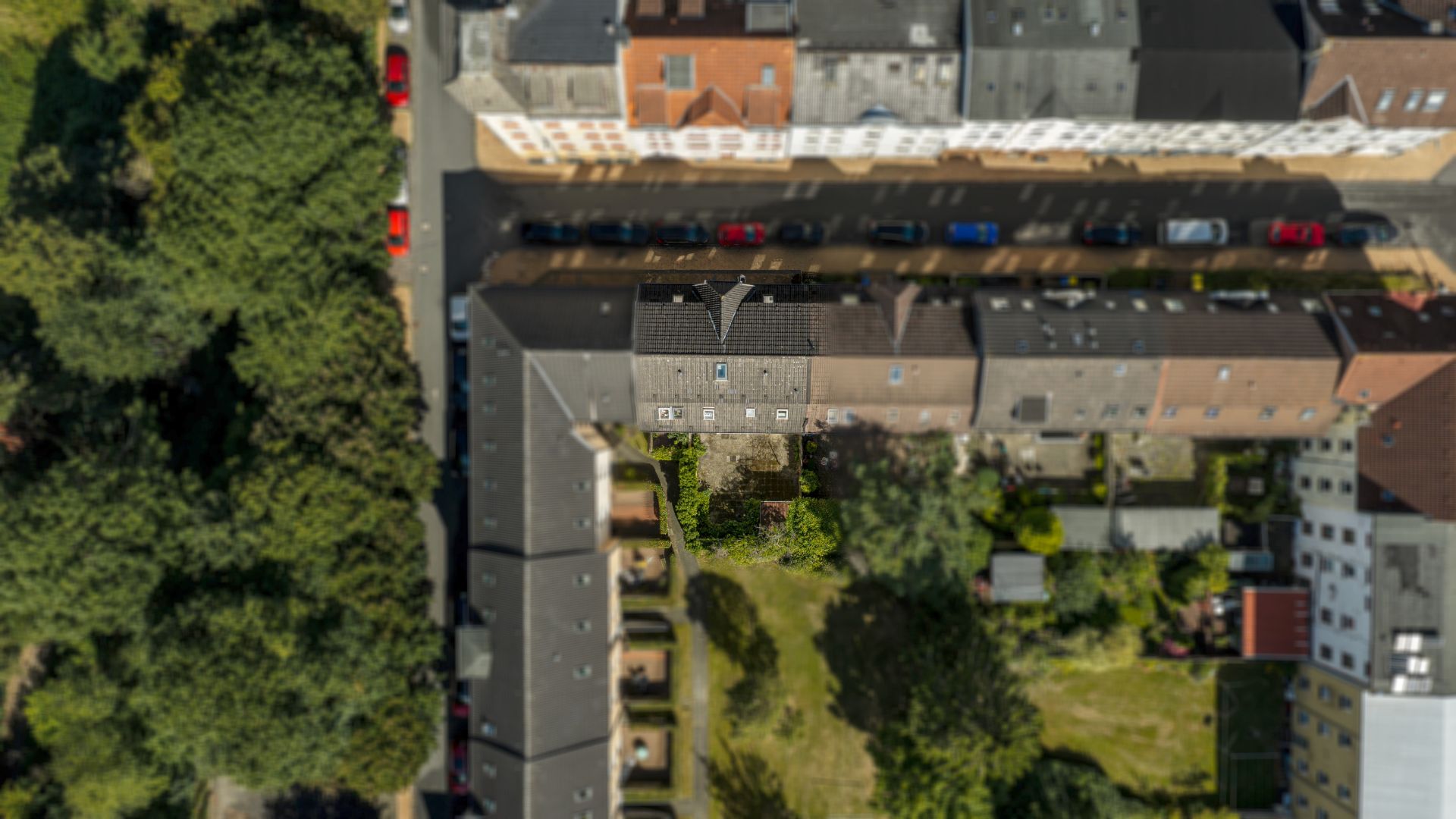 Luftaufnahme von Wohnhäusern mit Gärten und parkenden Autos an der Straße.