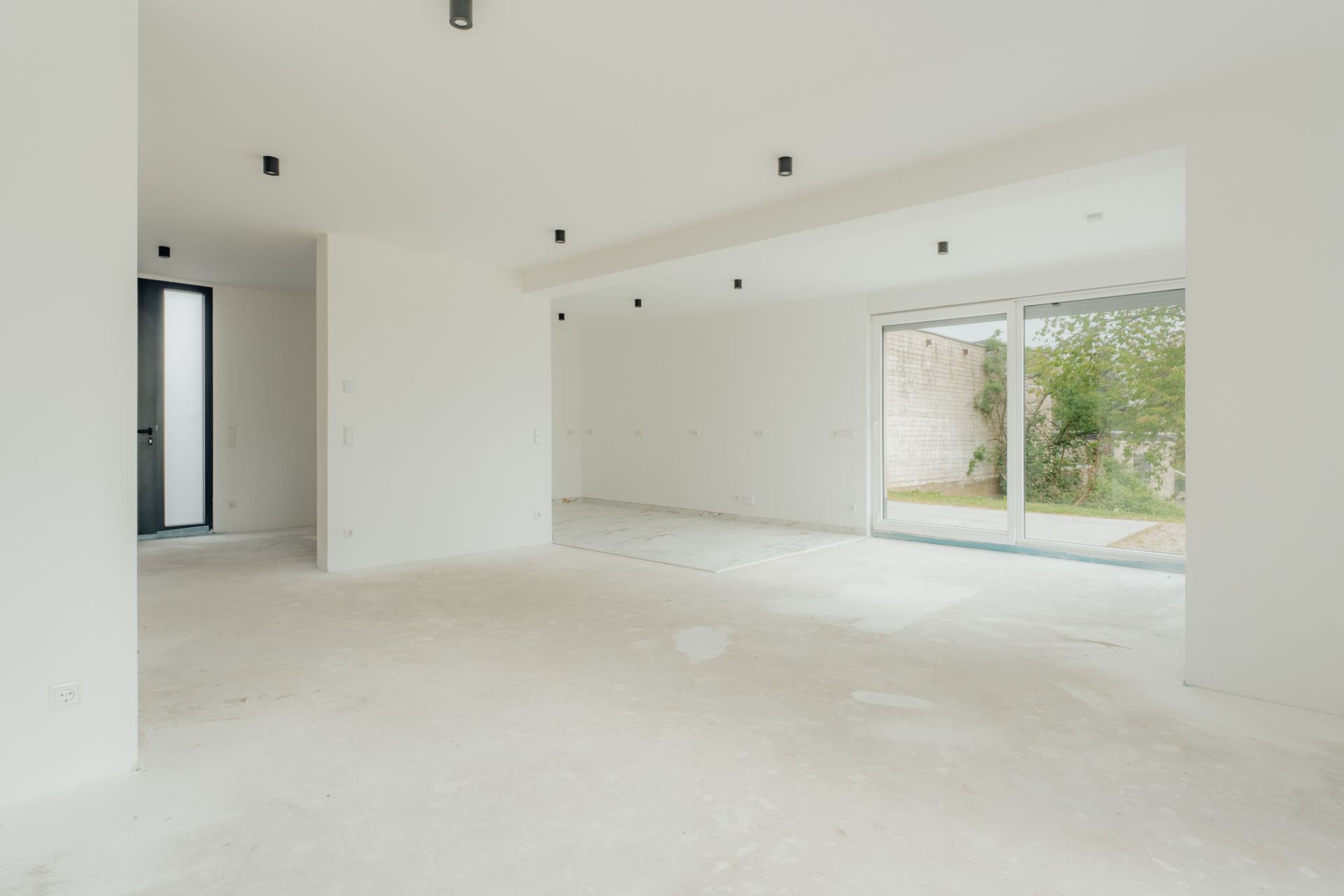 Helles, leeres Zimmer mit großen Fenstern und Schiebetür zum Garten.