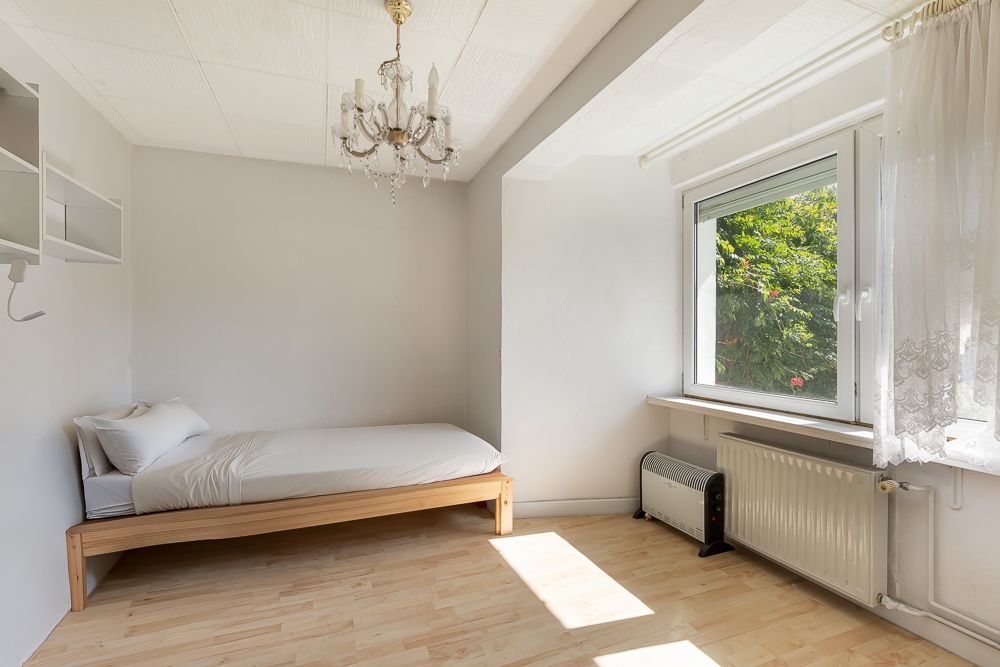 Helles Schlafzimmer mit Einzelbett, Fenster, Kronleuchter und Holzfußboden.