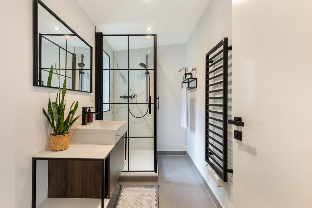 Modernes Badezimmer mit Dusche, Waschbecken, Spiegel, Handtuchhalter und Zimmerpflanze.