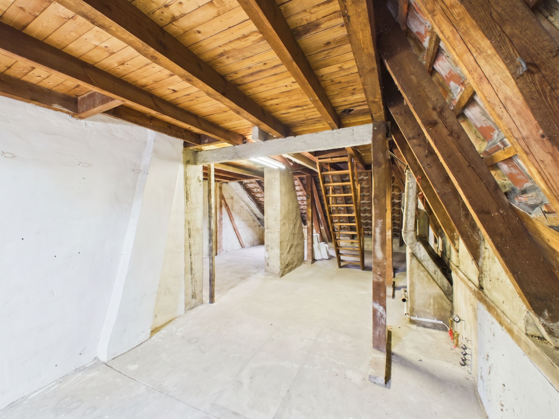 Unrenovierter Dachboden mit schrägen Holzbalken und sichtbarem Dachstuhl.