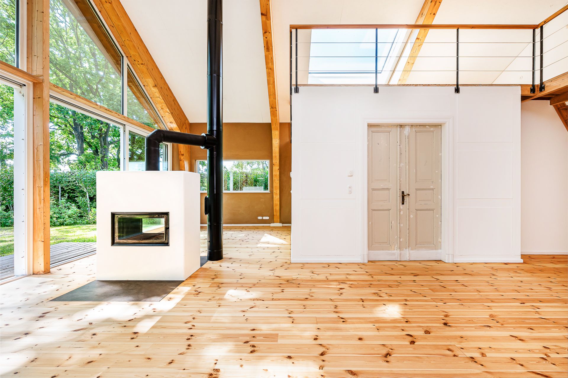 Helles Wohnzimmer mit Holzboden, Kamin und großen Fenstern mit Blick auf den Garten.