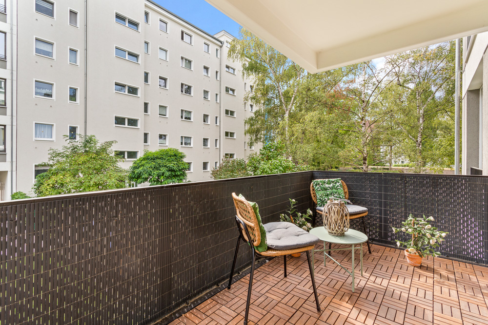 Balkon mit zwei Stühlen, Tisch und Pflanzen, Blick auf Bäume und Wohngebäude.