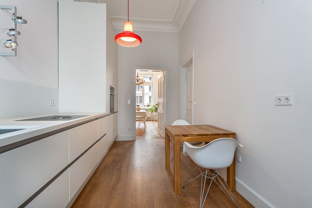 Moderne Küche mit Holzfußboden, Esstisch und weißen Stühlen, rote Lampe an der Decke.