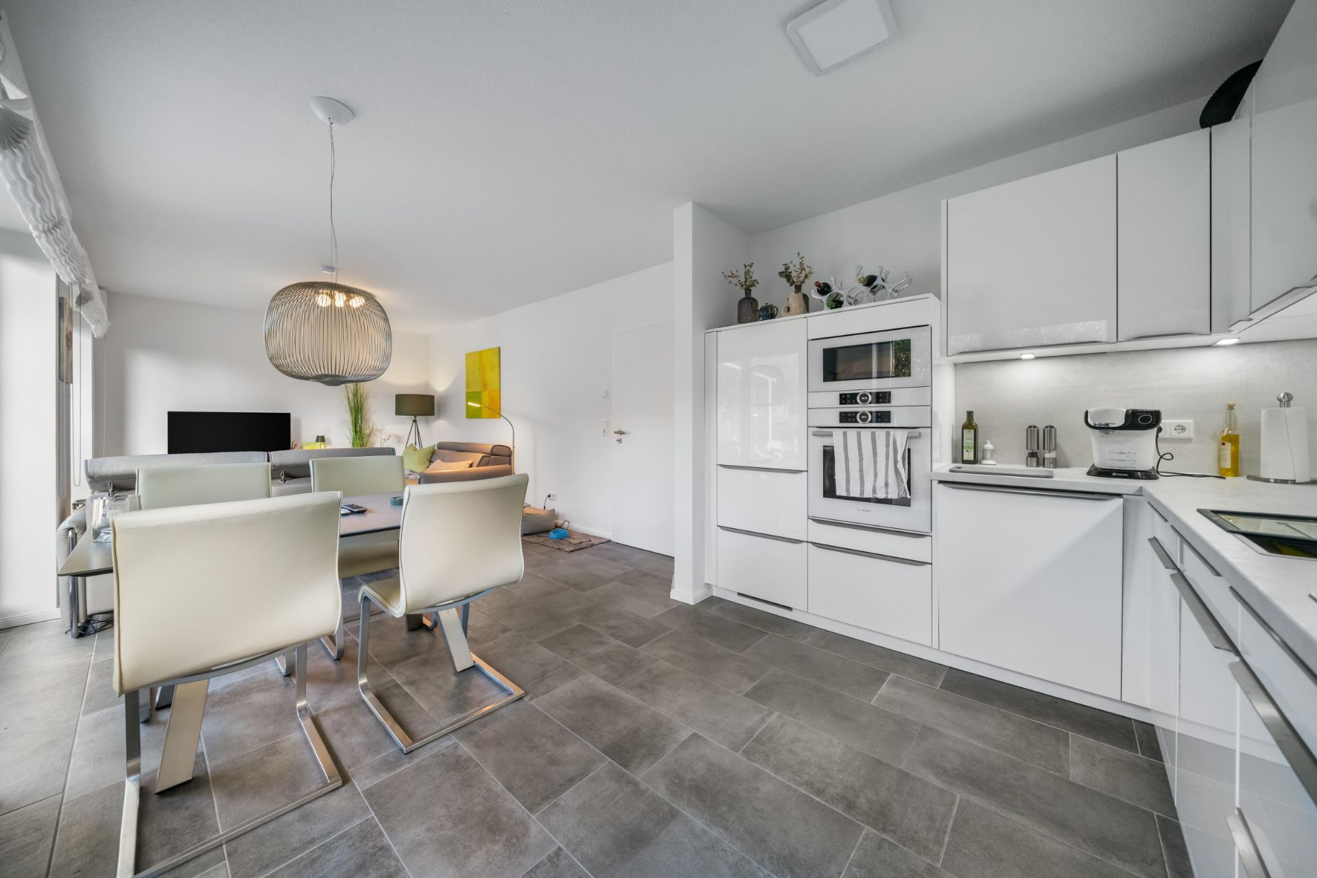 Moderne Küche mit Essbereich und Wohnzimmer, große Fenster und weiße Möbel.