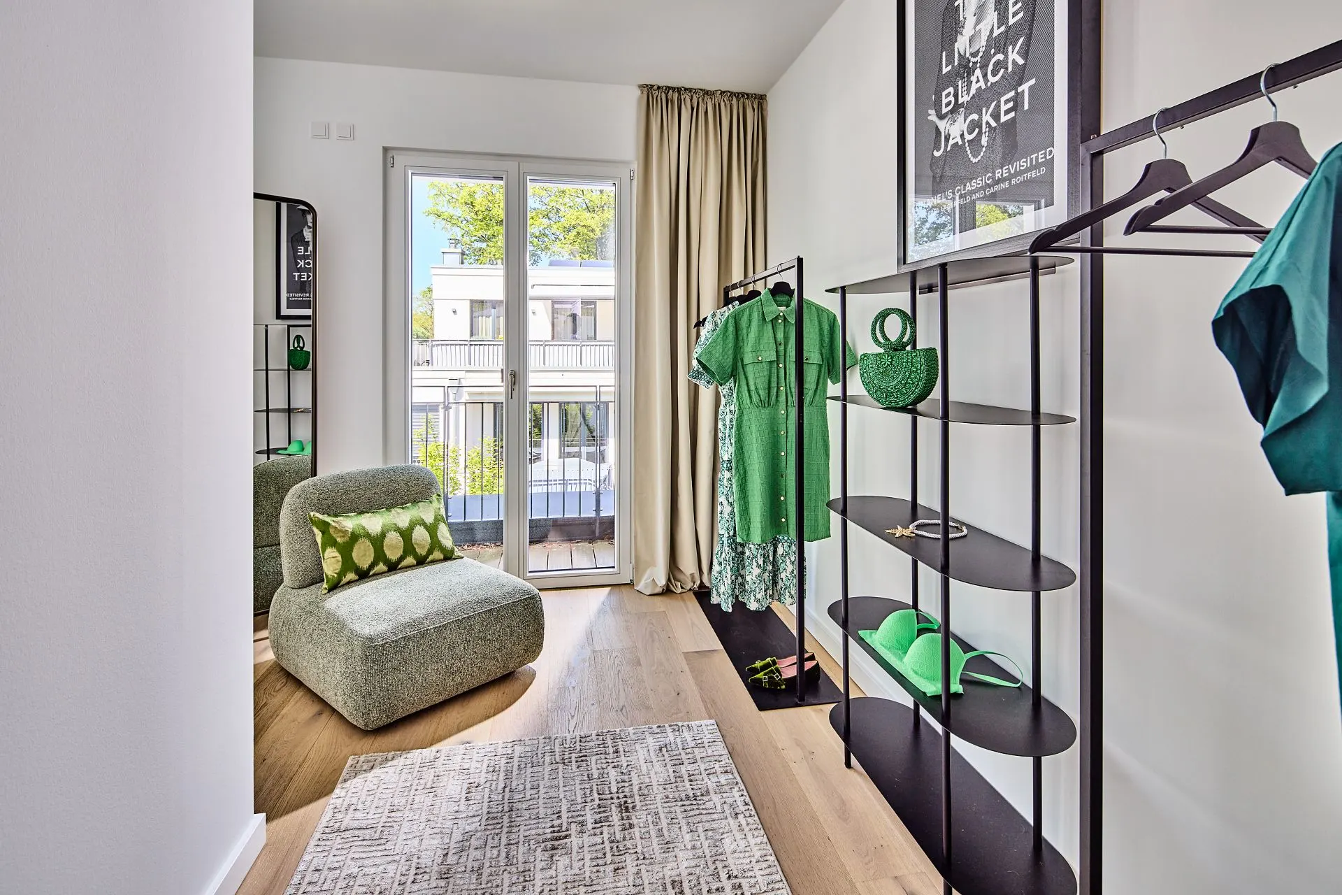 Heller Raum mit Sessel, Teppich, Regal, grüner Kleidung und Zugang zu einem Balkon.