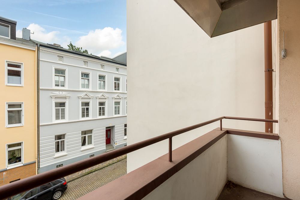 Balkon mit braunem Geländer, Blick auf Wohnhäuser und eine ruhige Straße.