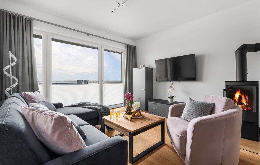Modernes Wohnzimmer mit Sofa, Sessel, Kamin, Couchtisch und großem Fenster mit Vorhängen.