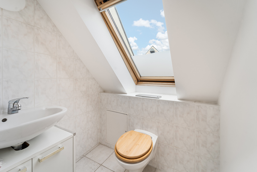 Kleines Badezimmer mit Waschbecken, Toilette und Dachfenster mit Blick auf den Himmel.
